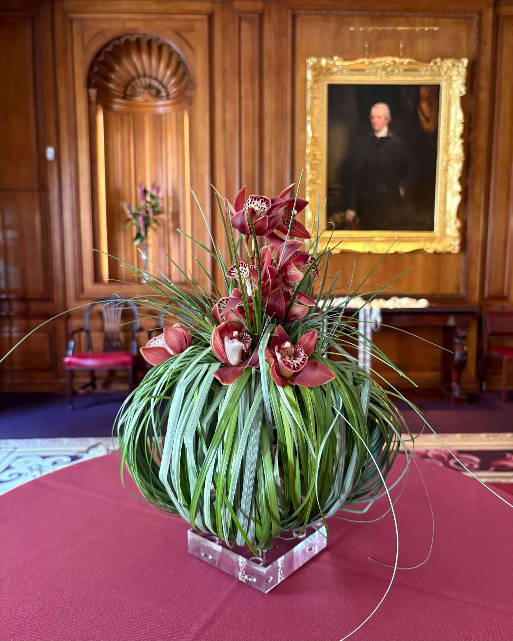 Bear grass and cymbidium orchids on an acrylic pedestal