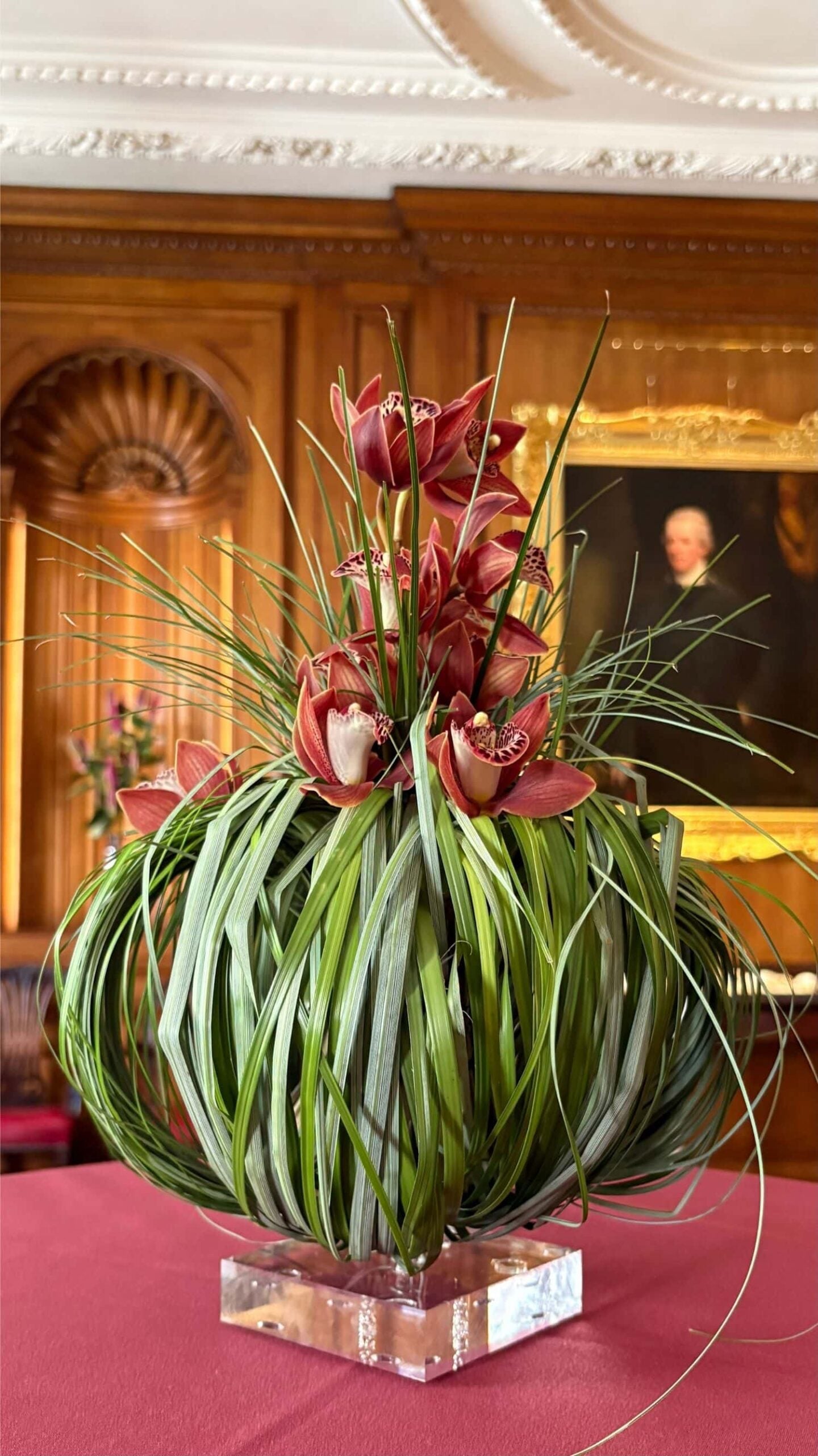 Bear grass and cymbidium orchids on an acrylic pedestal